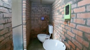 A small, narrow bathroom with a brick wall, a toilet, and a sink. - Hotel O Naga Puri Beach Retreat (Kuala Penyu)