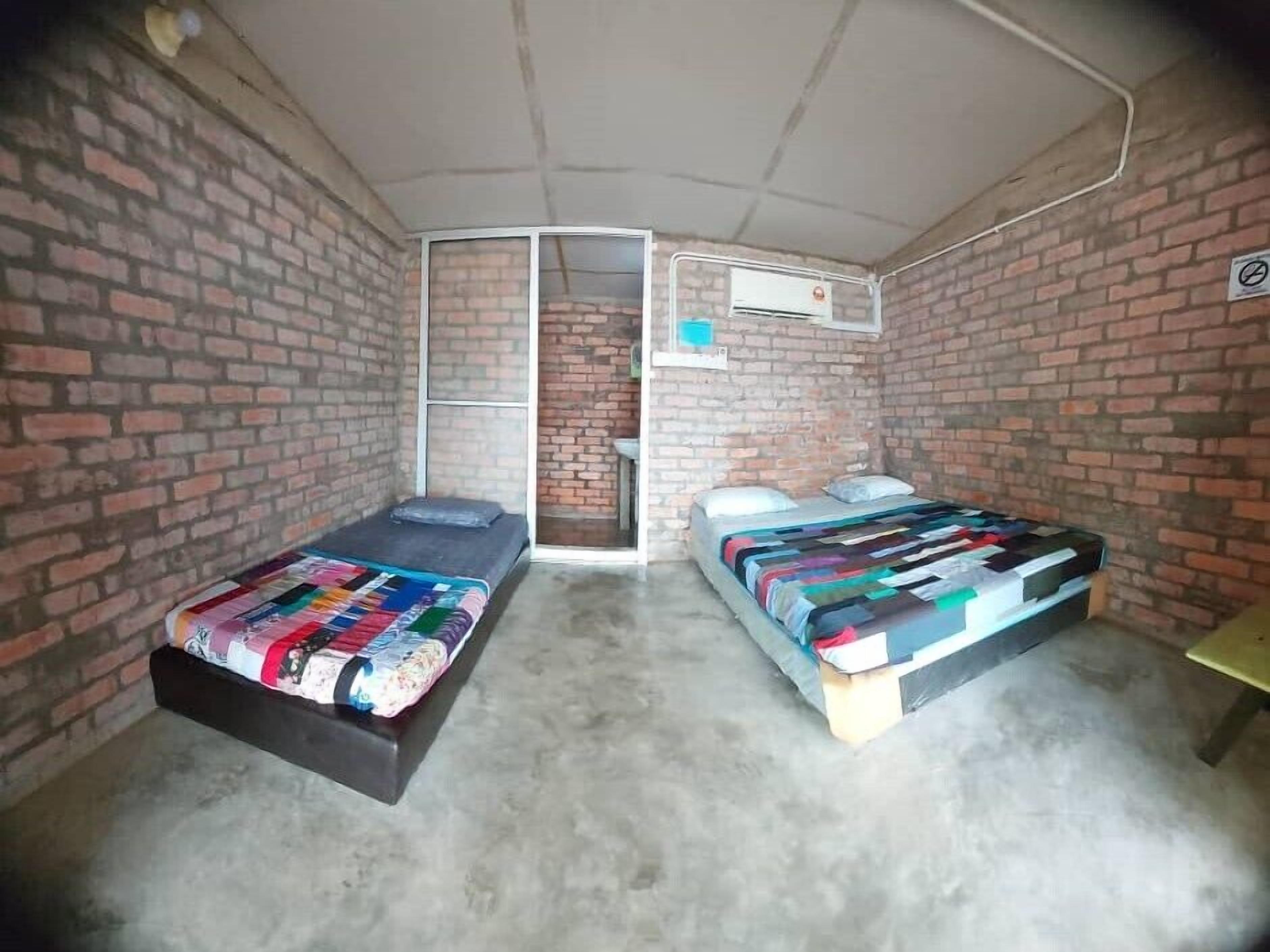 A small, enclosed room with two beds, a brick wall, and an air conditioning unit.