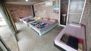 Quarto com duas camas, parede de tijolos, janela e pia.