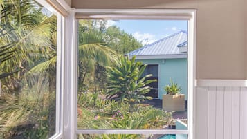 Relax in a serene room with a view of lush greenery and the swimming pool, featuring a comfortable bed and a stylish bathrobe.