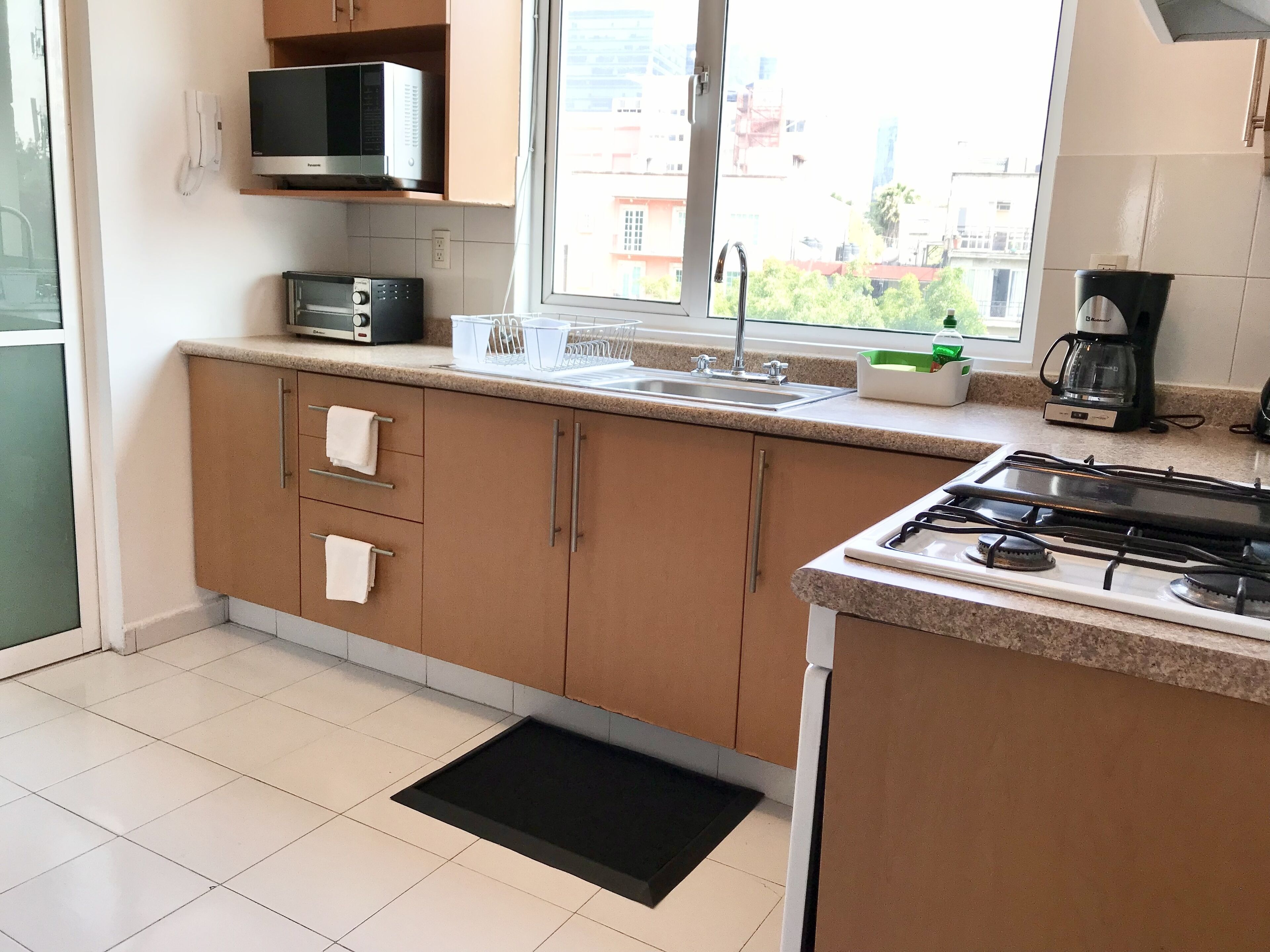 A modern kitchen with a microwave, stove, sink, and window with a view of buildings.