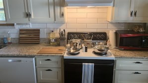 A kitchen with white cabinets, a stove, a microwave, and a wooden cutting board. - Lake Cabin with Fantastic View--Kayak, Swim or Fish (Perryville)