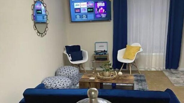 Ein Wohnzimmer mit einer Couch, zwei Sesseln, einem Couchtisch, einem Fernseher und einem dekorativen Gegenstand im Vordergrund.