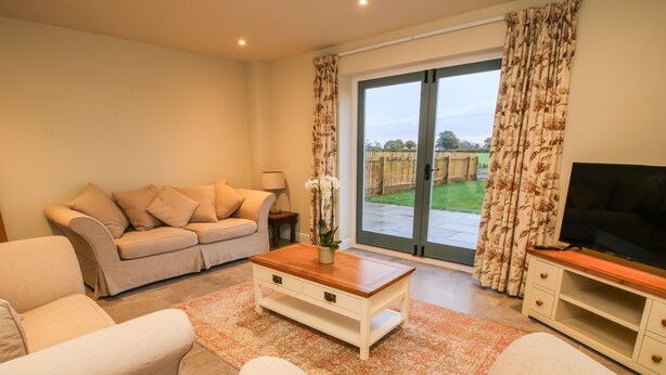 A living room with a sofa, coffee table, TV stand, and a sliding glass door leading to a garden. - The Barn (Shrewsbury)