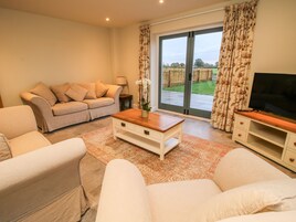 Una sala de estar con sofá, mesa de centro, mueble para TV y puerta corrediza de vidrio que da a un jardín.