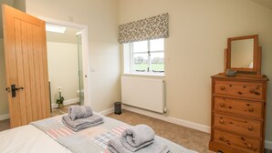 A bedroom with a bed, a dresser, a window with a view, and a door leading to another room. - The Barn (Shrewsbury)
