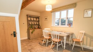 A dining area with a wooden table and white chairs, a cabinet with decorative plates, and a window with a view of greenery. - The Barn (Shrewsbury)