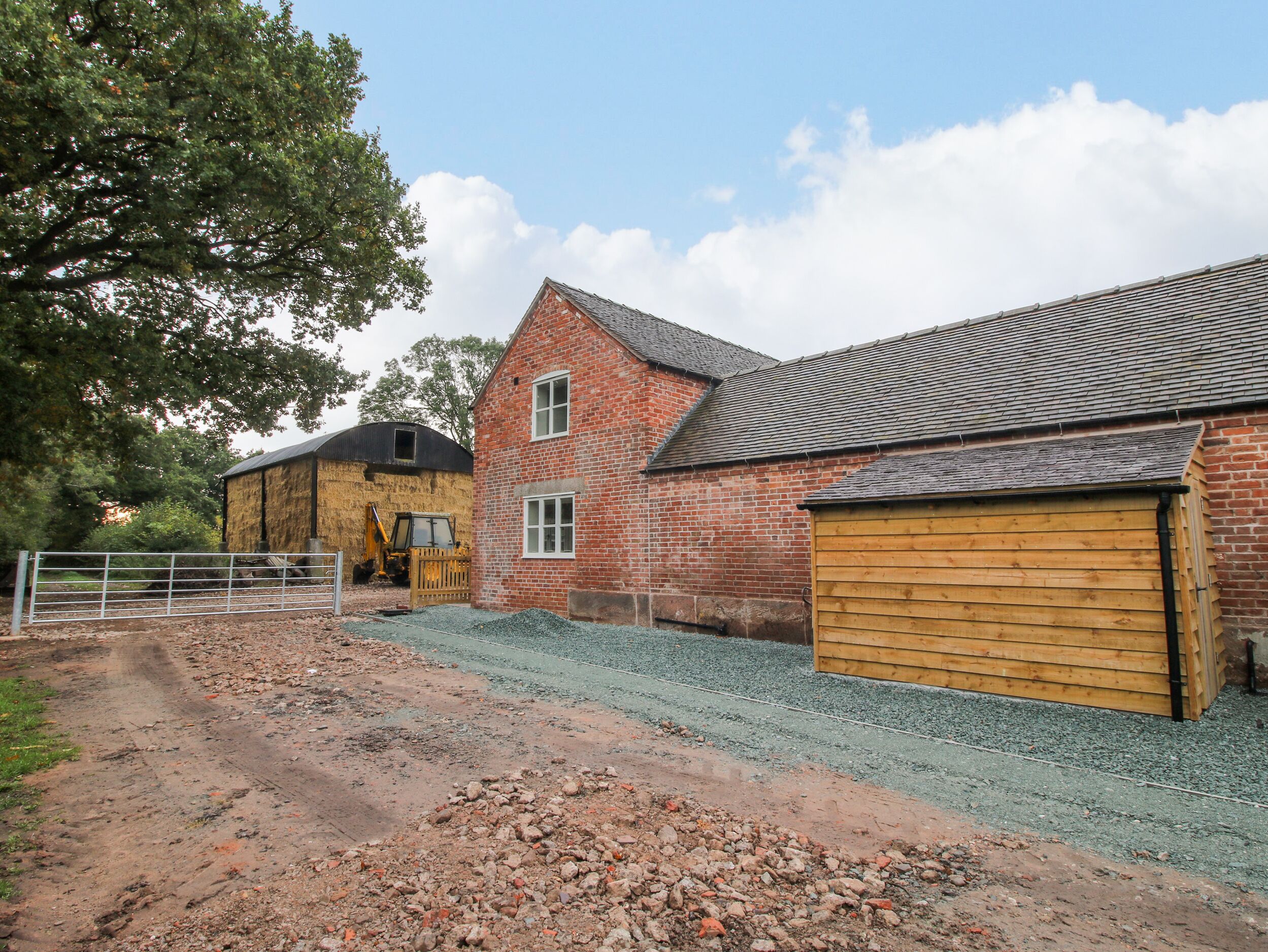A rural barn with a dirt path leading to it, surrounded by gravel and a metal fence.