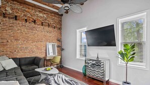 A living room with a brick wall, a sofa, a TV, a plant, and a modern console table. - DC’s Southwest and Navy Yard Welcomes You! (Washington)