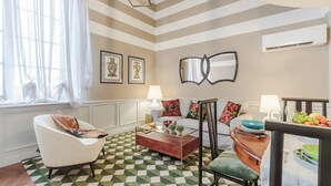 A living room with a checkered floor, a sofa, a coffee table, and a dining area with a fruit bowl and glasses.
