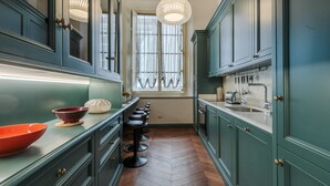 A narrow kitchen with dark green cabinets, a wooden herringbone floor, and a long bar stool line.