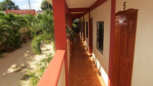 A corridor with a tiled floor, wooden doors, and a red railing. - Hotel NICTE HA (Xpujil)