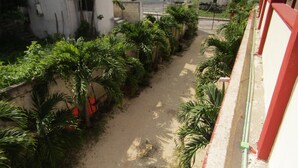 A narrow pathway flanked by lush greenery and a building with a red and white facade. - Hotel NICTE HA (Xpujil)