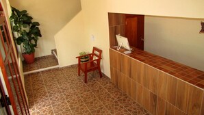 A reception area with a wooden counter, a chair, a potted plant, and a ceiling fan. - Hotel NICTE HA (Xpujil)
