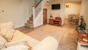 A living room with a staircase, a flat-screen TV, a dining area with chairs, and a wooden bench. - Cow'ouse (Shrewsbury)