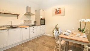 A modern kitchen with white cabinets, a wooden countertop, and a dining area with a wooden table and chairs. - Cow'ouse (Shrewsbury)