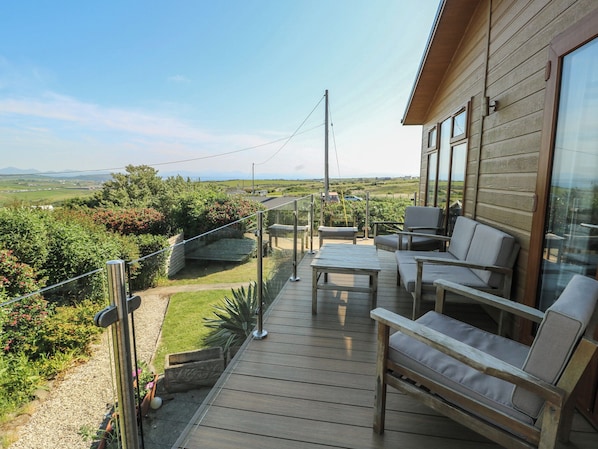 A wooden deck with outdoor furniture, a glass railing, and a view of the countryside.