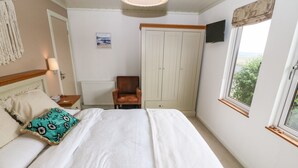 A bedroom with a bed, a chair, a wardrobe, a radiator, a painting, and a window with a view.
