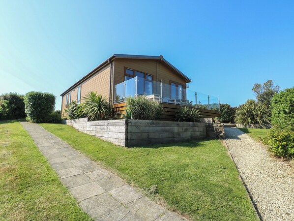 A single-story house with a paved driveway, a wooden deck, and a well-maintained lawn. - Sunstone Lodge (Pwllheli)