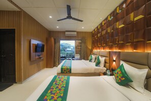 A hotel room with two beds, a TV, a ceiling fan, and a view of the outdoors. - Treebo Iceberg 700Meters From Venna Lake (Mahabaleshwar)