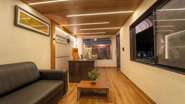 A reception area with a wooden ceiling, a reception desk, a black leather couch, and a small wooden table with a plant. - Treebo Iceberg 700Meters From Venna Lake (Mahabaleshwar)