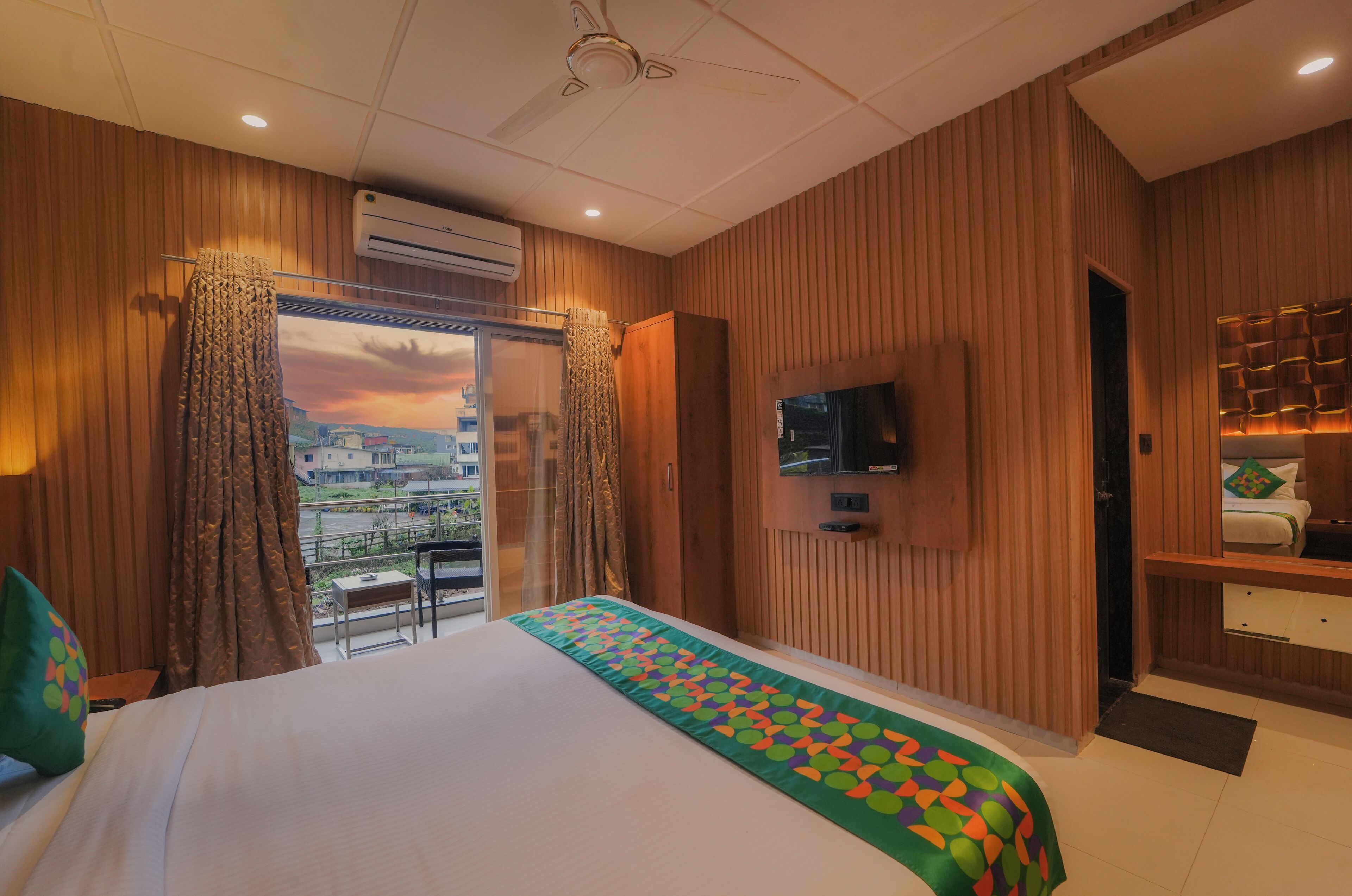 Ein Hotelzimmer mit einem großen Bett, einem an der Wand montierten Fernseher und einem Balkon mit Vorhängen.