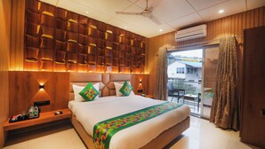 A modern hotel room with a large bed, a wooden headboard, a ceiling fan, and an air conditioning unit. - Treebo Iceberg 700Meters From Venna Lake (Mahabaleshwar)