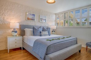 Een slaapkamer met een bed, nachtkastjes, een raam met jaloezieën en kunst aan de muur.