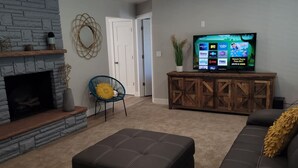 A living room with a stone fireplace, a television on a wooden cabinet, a blue chair, and a brown sofa. - Updated 4-bedroom home centrally located in Logan (Logan)