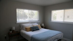 A bedroom with a bed, two bedside tables, a nightstand, and a window with blinds. - Updated 4-bedroom home centrally located in Logan (Logan)