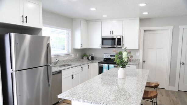 A modern kitchen with white cabinets, stainless steel appliances, granite countertops, and a central island with bar stools. - Updated 4-bedroom home centrally located in Logan (Logan)
