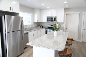 Una cocina moderna con armarios blancos, electrodomésticos de acero inoxidable, encimeras de granito y una isla central con taburetes de bar.