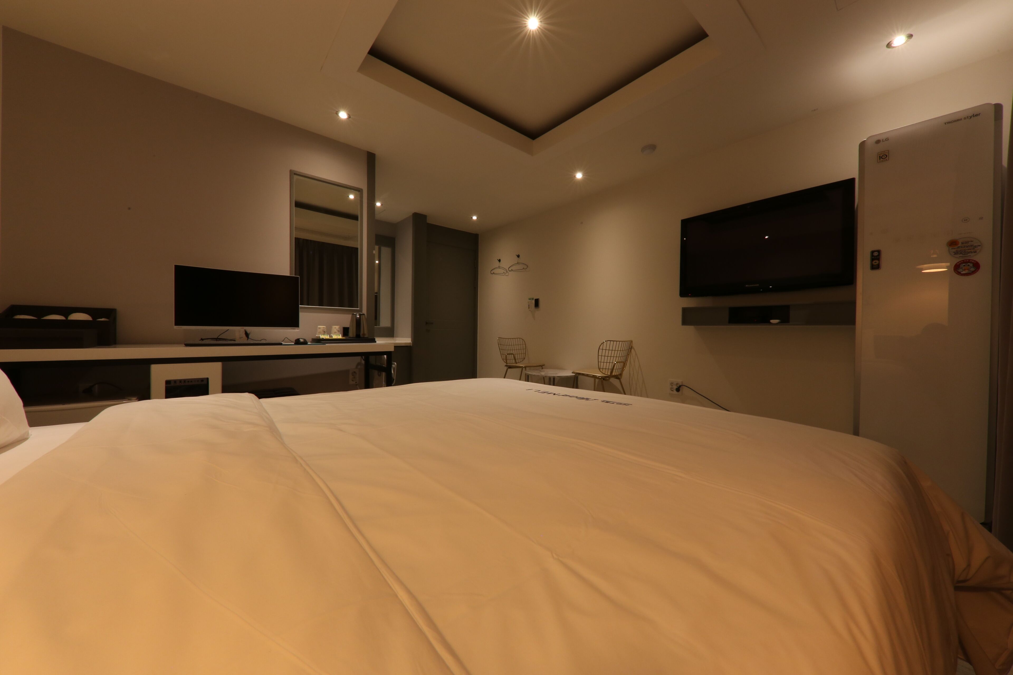 Una habitación de hotel moderna con una cama grande, un televisor de pantalla plana montado en la pared, un escritorio con computadora y un refrigerador.