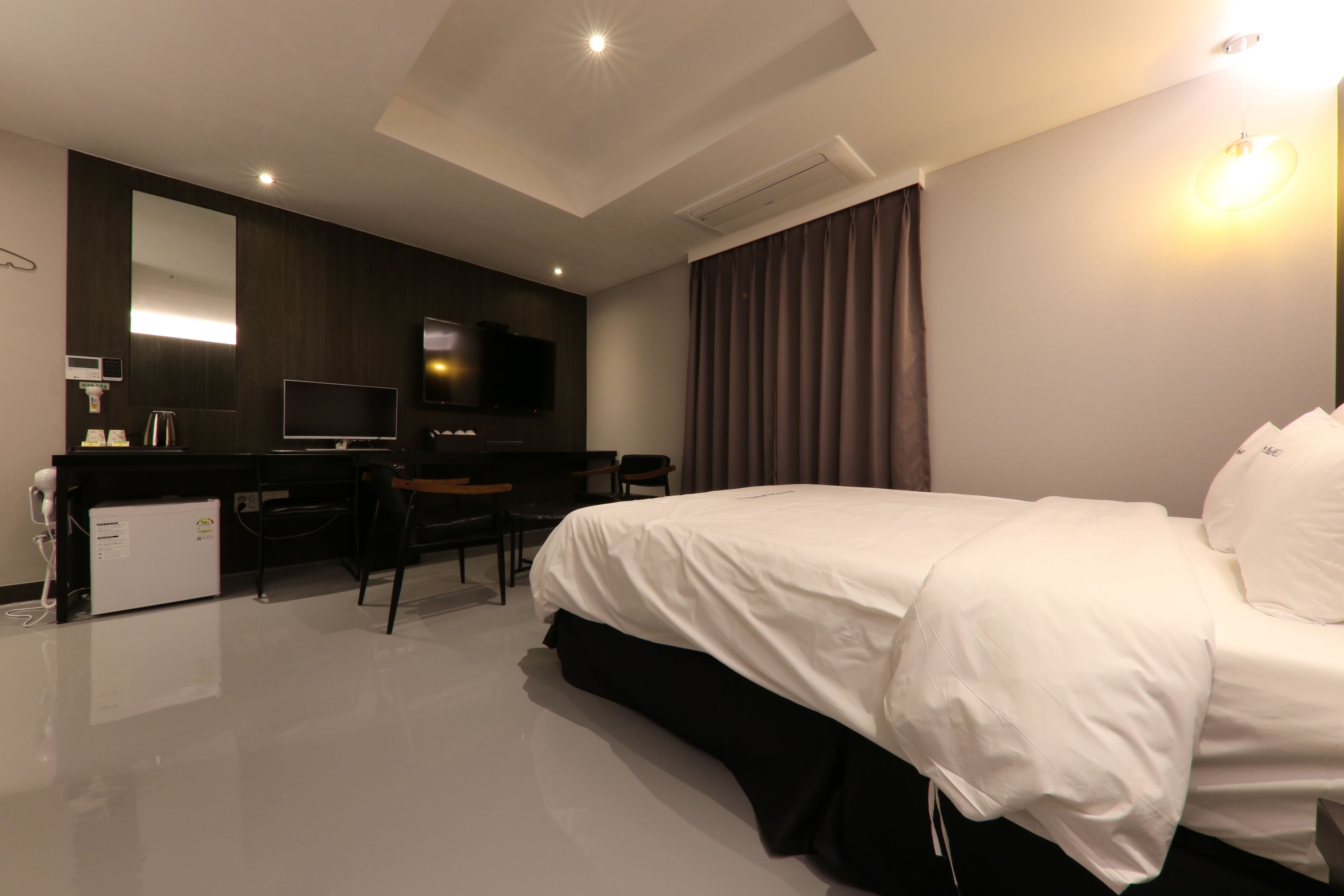 Quarto de hotel moderno com uma cama grande, uma escrivaninha, uma TV de tela plana, um mini-bar e um espelho amplo.