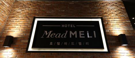 Un letrero de hotel con el nombre 'MeadMELI' sobre una pared de ladrillo.