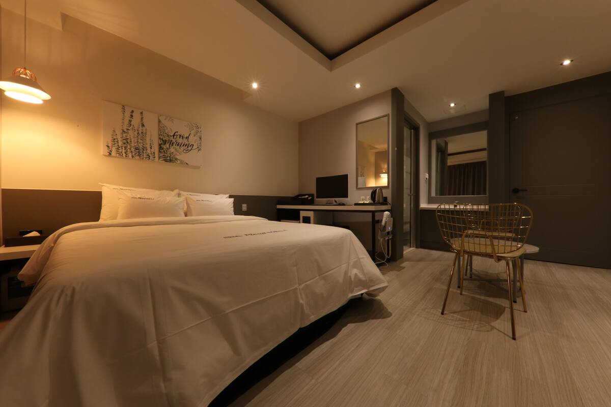Una habitación de hotel moderna con una cama grande, un escritorio, una silla y un espejo.