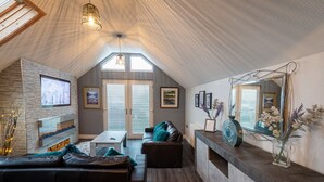A cozy loft-style living room with a fireplace, a large mirror, and a dining area. - Lakeland Lodge (Carnforth)