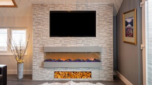 A modern living room with a flat-screen TV mounted on a textured wall, a fireplace with logs, a fluffy rug, and a decorative vase with branches. - Lakeland Lodge (Carnforth)