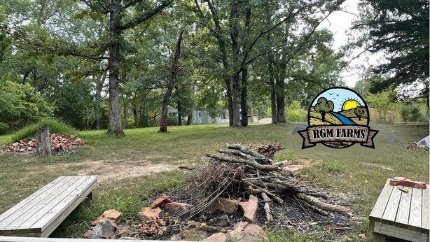 Ein Campingplatz mit einem Holzstapel, zwei Holzbänken und dem Logo von RGM Farms.