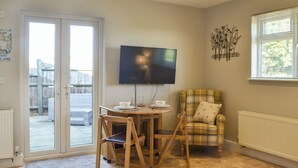 Una sala de estar acogedora con comedor, televisor montado en la pared y una ventana con persianas.