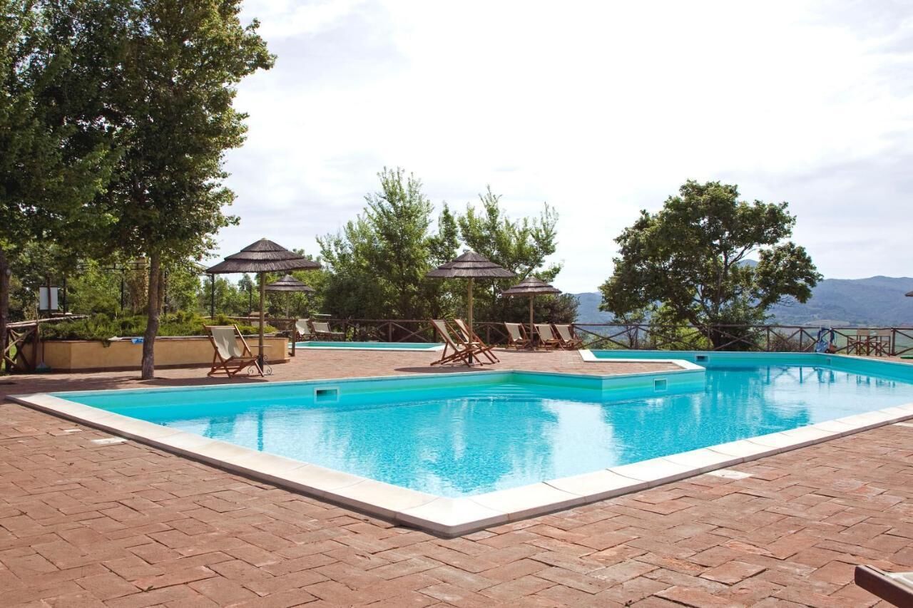 Ein rechteckiger Pool mit einer gefliesten Kante, umgeben von einer Pflasterterrasse. Liegestühle und Sonnenschirme befinden sich rund um den Pool.