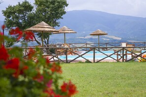 A poolside area with umbrellas, lounge chairs, and a view of mountains.