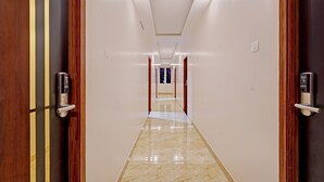 Passadís modern d'hotel amb portes de fusta, terra de marbre i vista cap a la zona de recepció al final.