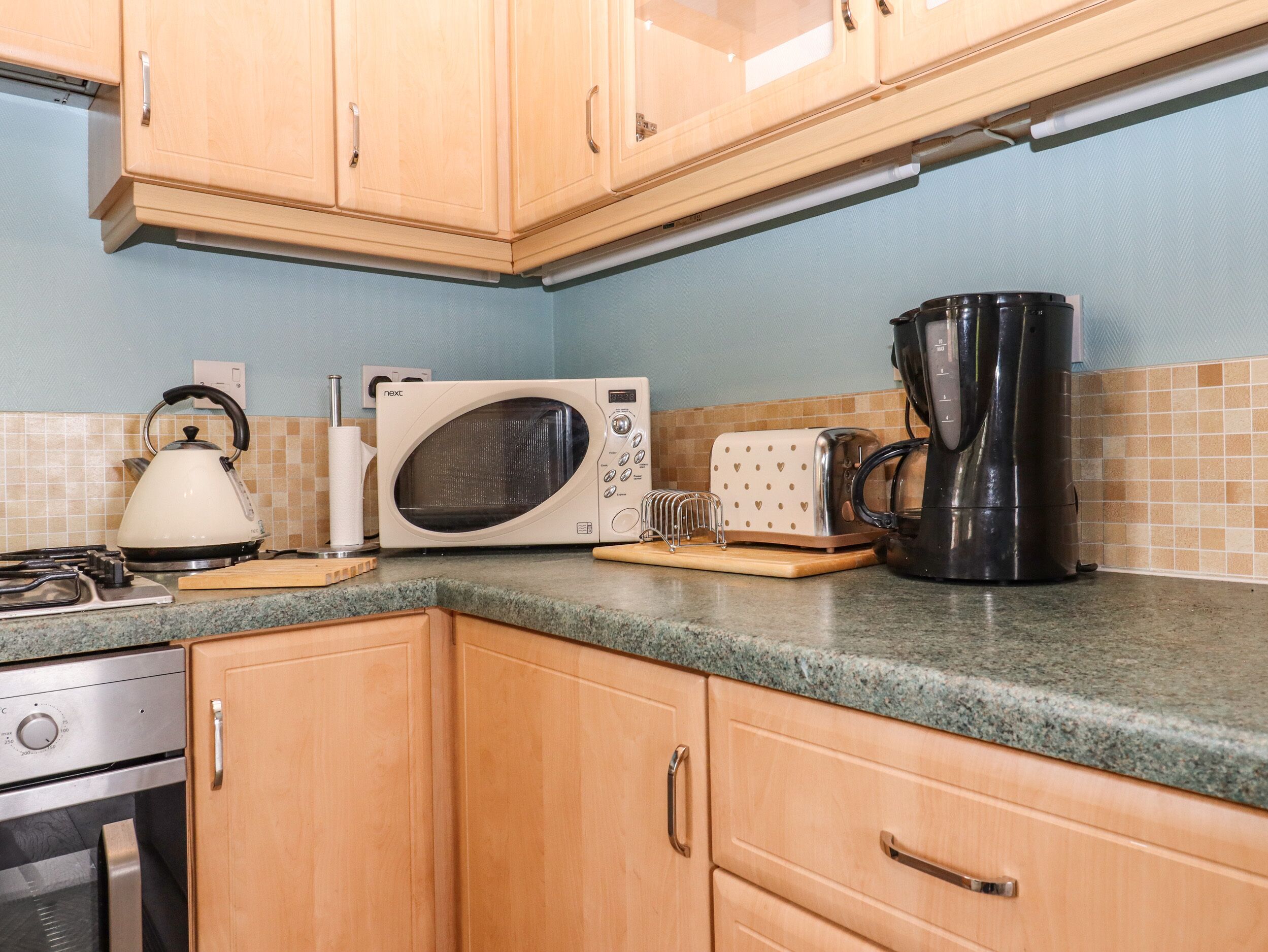 A kitchen with wooden cabinets, a microwave, a kettle, a toaster, and a coffee maker.