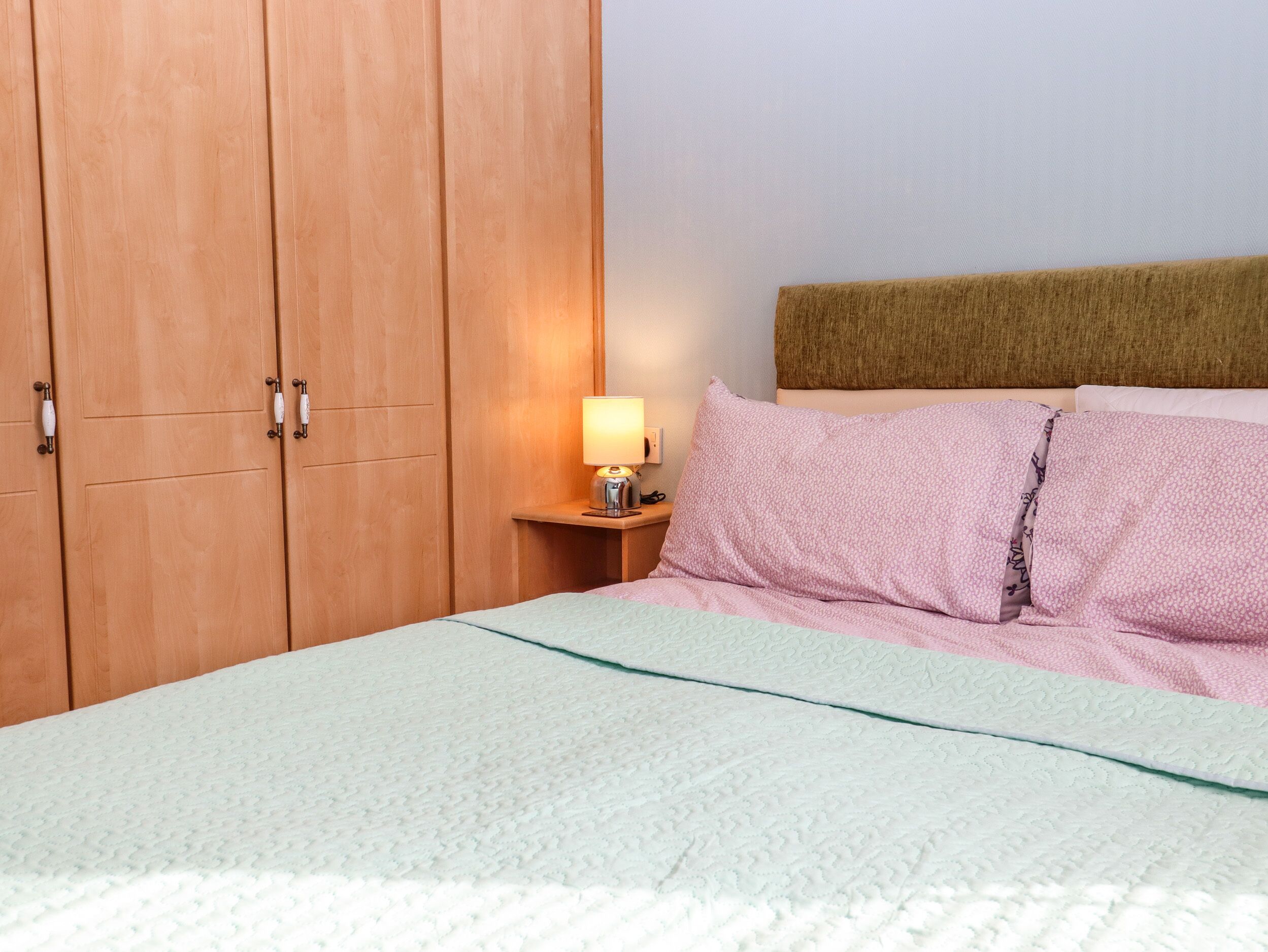 A bedroom with a bed, a nightstand with a lamp, and wooden wardrobe doors.