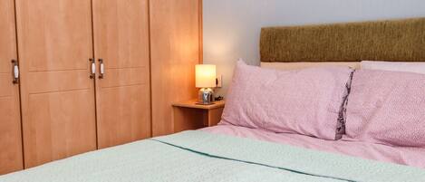 A bedroom with a bed, a nightstand with a lamp, and wooden wardrobe doors.