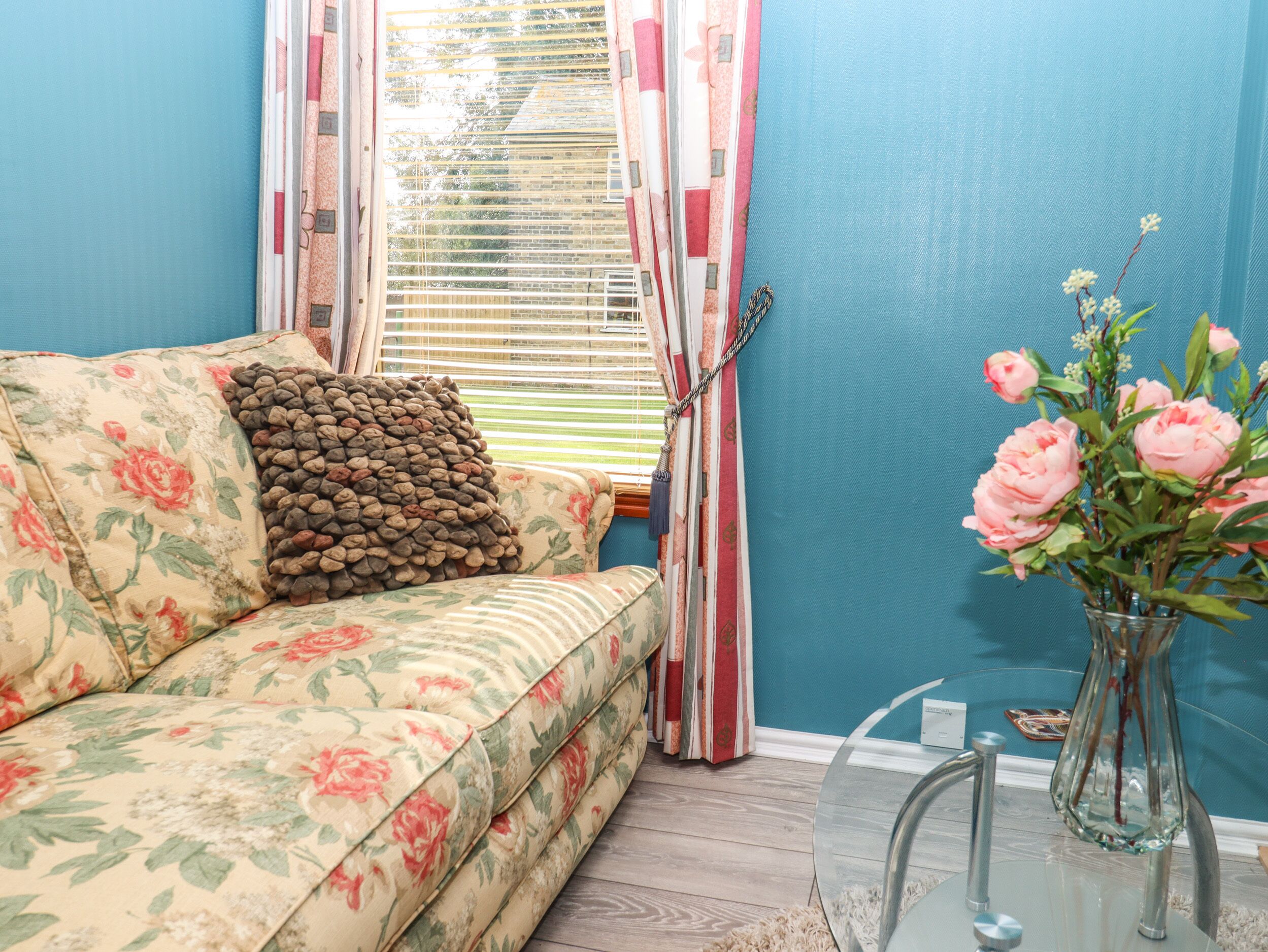 Et værelse med en blomstret sofa, en vase med blomster og et vindue med gardiner.