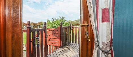 A wooden deck leading to a gate with a view of greenery and a clear sky.