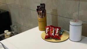 Un comptoir de cuisine avec une machine à café, un bocal de dosettes de café, un paquet de collations et un récipient blanc.