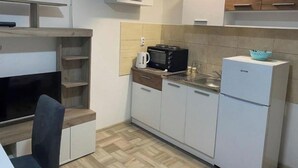 Une cuisine compacte avec des meubles blancs, un four à micro-ondes, une bouilloire et un petit réfrigérateur.